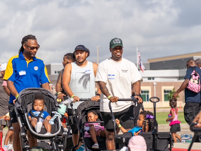 Dads pushing strollers together at a community walk